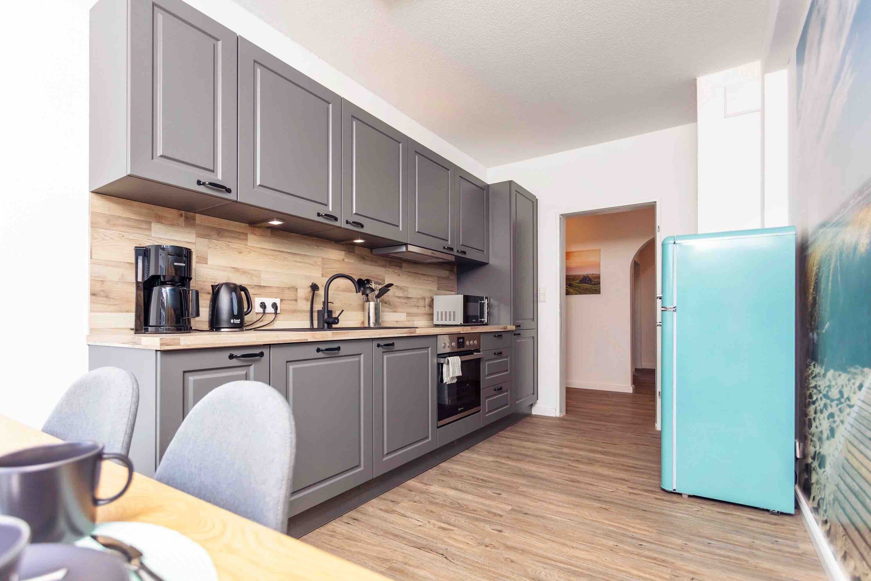 A modern kitchen with grey cabinets, a wooden countertop, and a teal refrigerator.