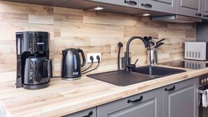 A modern kitchen with a wooden backsplash, a coffee maker, a kettle, a sink, and a microwave. - Apartment 'Büsumer Butze' with Private Garden and Wi-Fi (Büsumer Deichhausen)