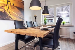 Un espace repas avec une table en bois, des chaises noires et des luminaires suspendus.