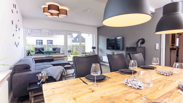 A modern dining area with a wooden table set for a meal, black chairs, and pendant lighting. - Apartment 'Büsumer Butze' with Private Garden and Wi-Fi (Büsumer Deichhausen)
