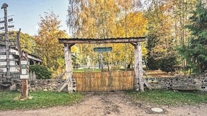 Ein rustikales Holztor mit einem Schild, umgeben von Bäumen und einer Steinmauer.