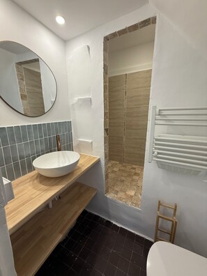 Un baño con lavamanos blanco, un espejo, ducha y toallero.