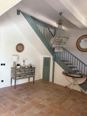 A staircase with a green railing, a chandelier, a mirror, and a dresser with drawers.