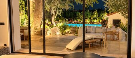 A modern living room with a large sliding glass door leading to an outdoor area with a pool and garden.