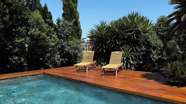 Una piscina rectangular con agua cristalina, rodeada por una terraza de madera y árboles.