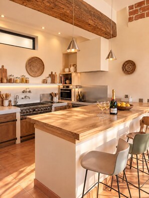 A modern kitchen with a large island, wooden ceiling beams, and pendant lighting.