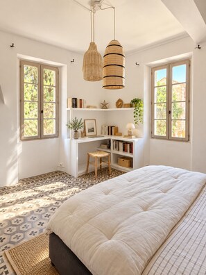 A bedroom with a bed, a desk, and two windows.