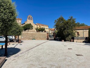 Un patio con un edificio de piedra que cuenta con un campanario, rodeado de árboles y automóviles estacionados.