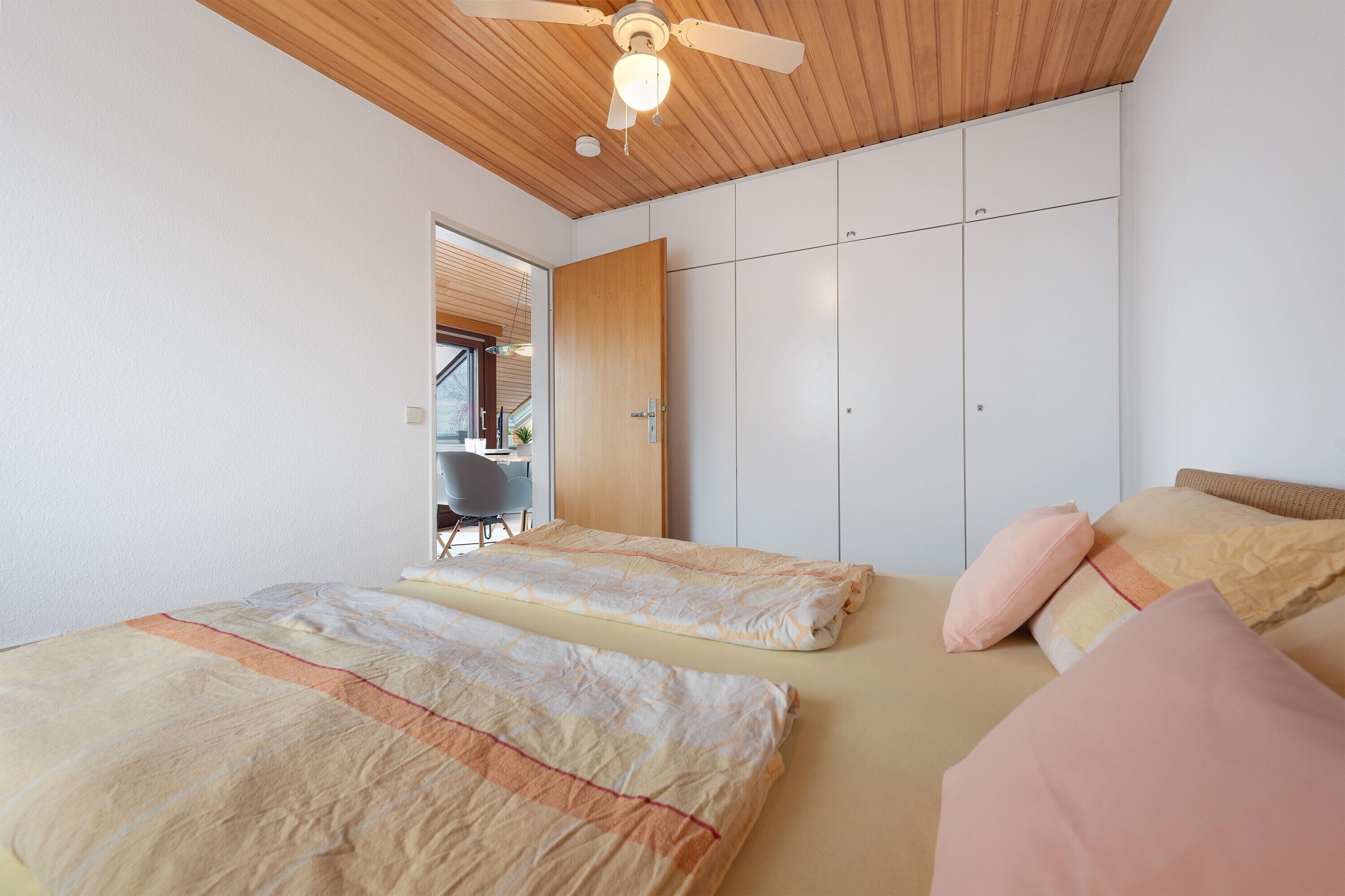 A bedroom with two beds, a ceiling fan, and a wardrobe.