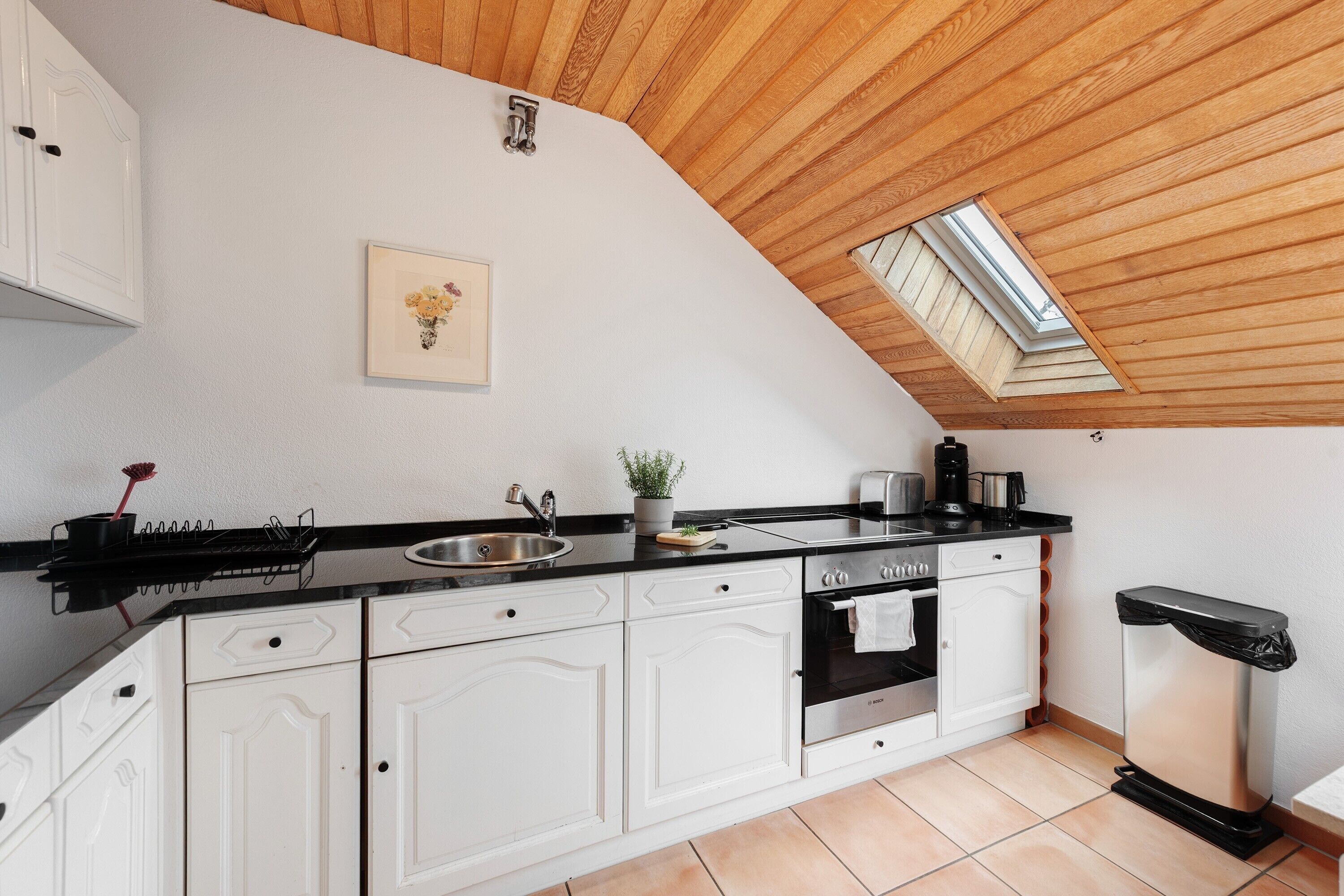 A kitchen with white cabinets, a black countertop, a skylight, and a stainless steel oven.