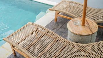 Un área junto a la piscina con sillones de mimbre y una mesa redonda con base de vidrio.