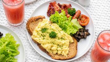 Un plato de desayuno con huevos revueltos, tocino, lechuga, tomates, champiñones y tostadas.