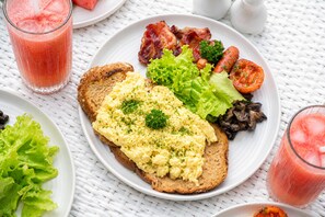 Un plato de desayuno con huevos revueltos, tocino, lechuga, tomates, champiñones y tostadas.