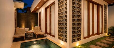A modern outdoor pool area with a built-in seating area, a stone wall, and a wooden ceiling.