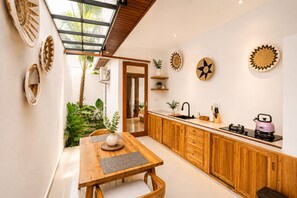 A modern kitchen with a wooden countertop, a sink, and a stove. There is a dining area with a table and chairs. - Arutala Private Villa (Ubud)
