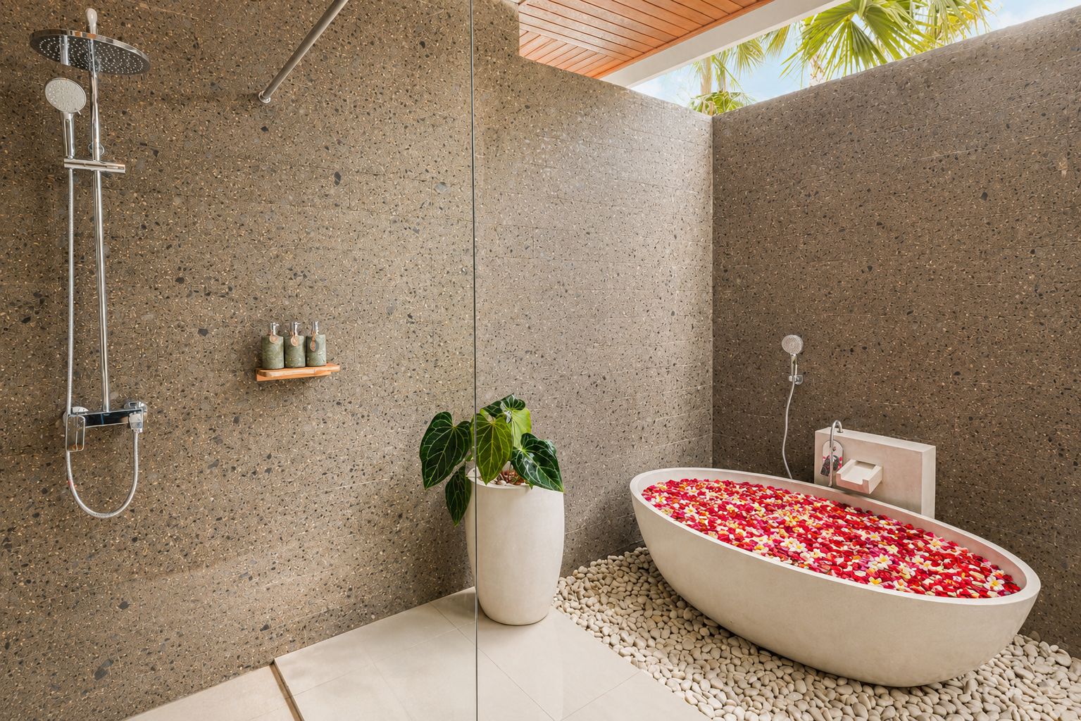 Un baño moderno con una bañera independiente llena de pétalos de rosa, una ducha y una planta en maceta.