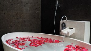 Een bad gevuld met water en rozenblaadjes, met een douchekop erboven.
