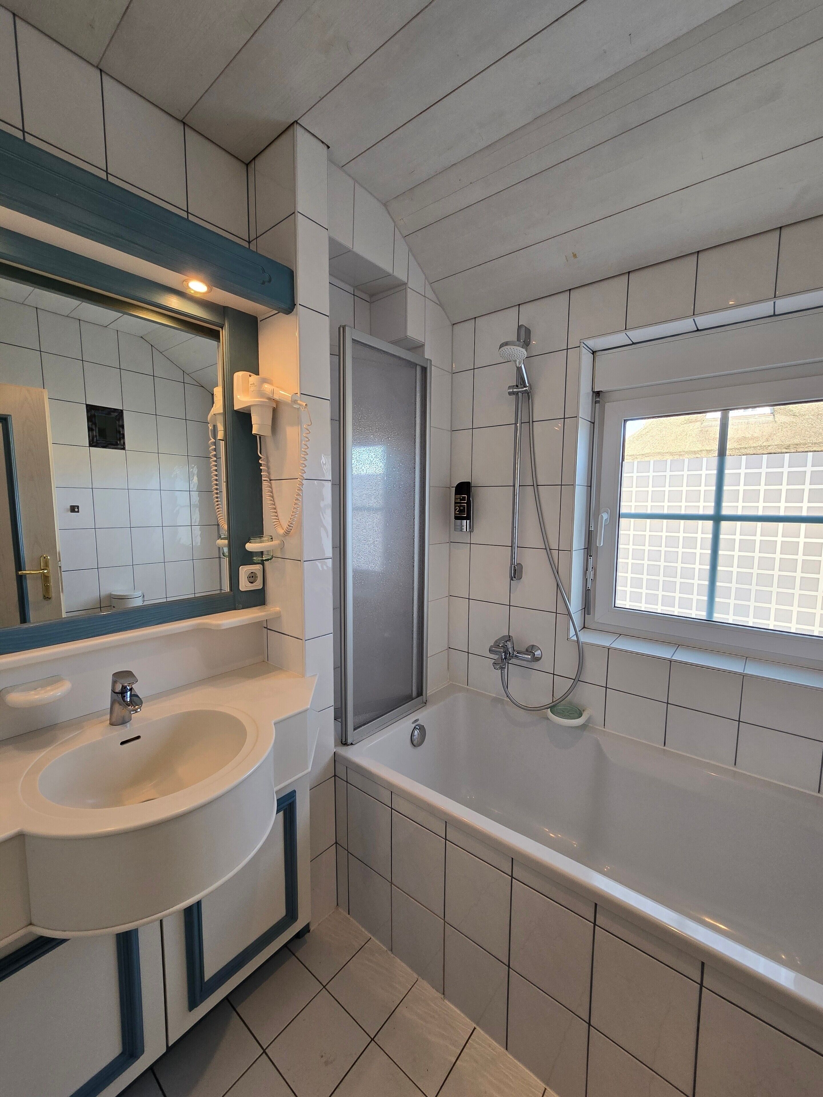 A bathroom with a sink, mirror, shower, and window.