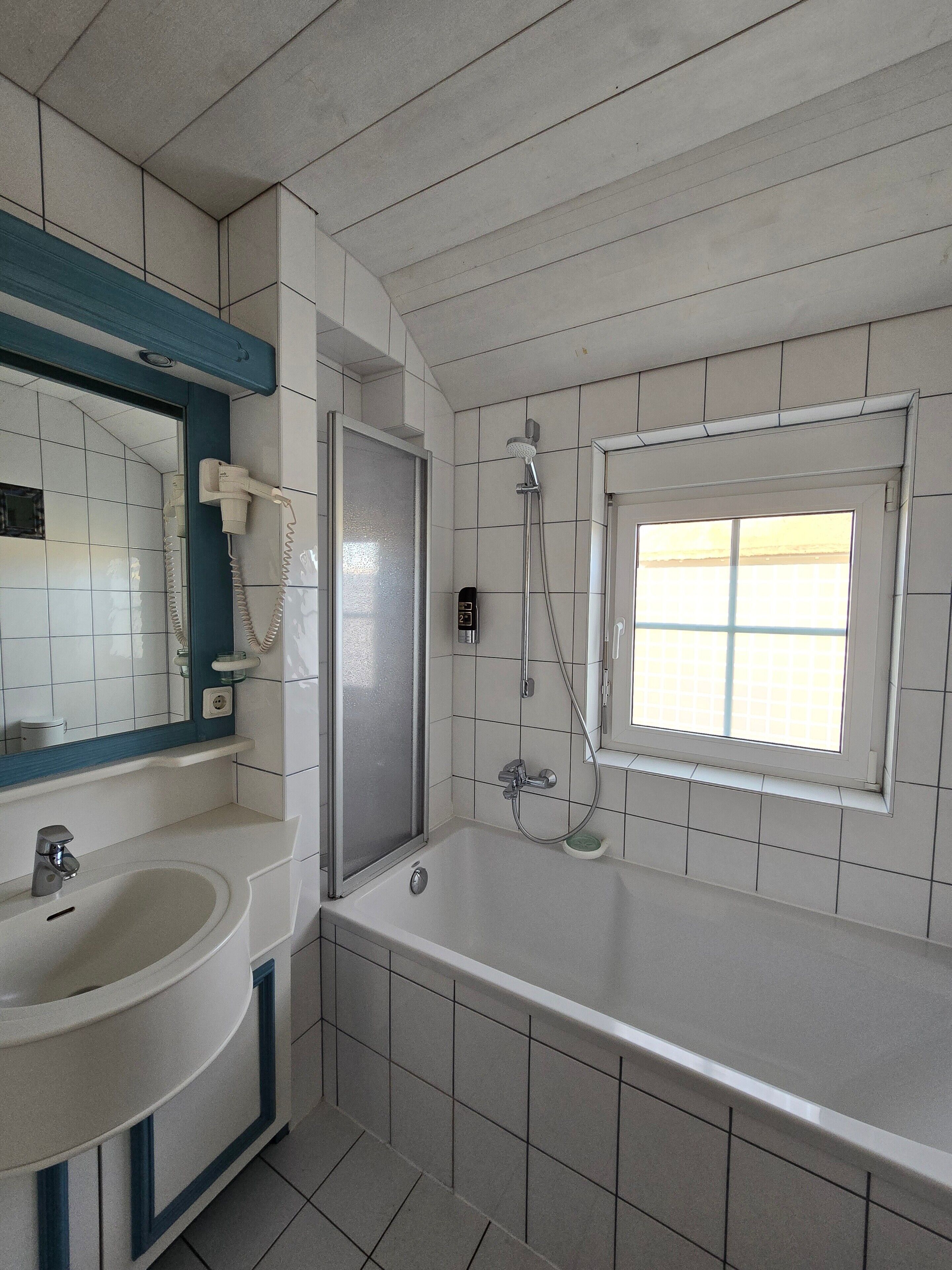 A bathroom with a bathtub, a shower, a sink, and a window.