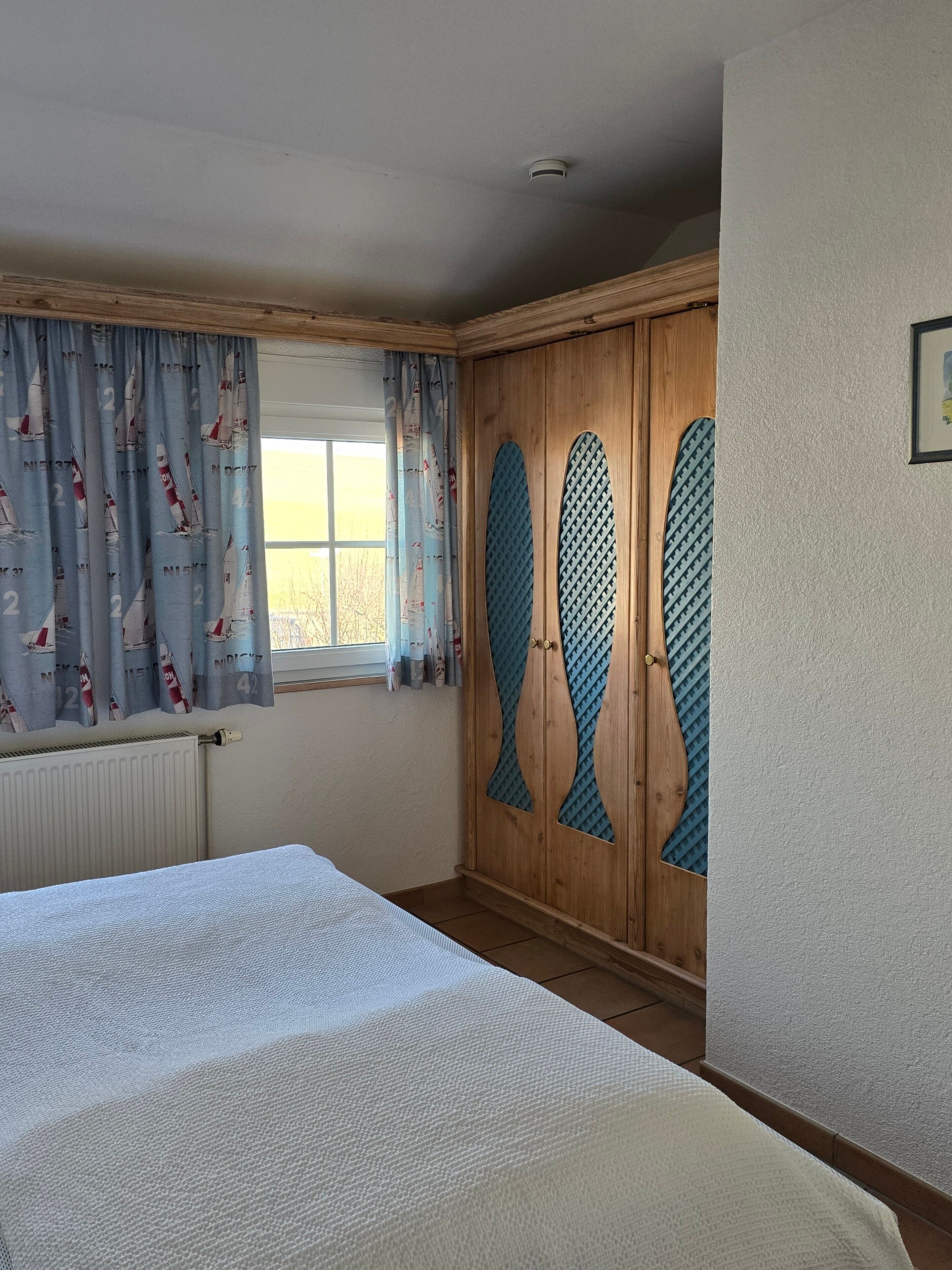 Ein Schlafzimmer mit einem Bett, einem Fenster mit Vorhängen, einem Heizkörper und einem Kleiderschrank mit individuellem Design.