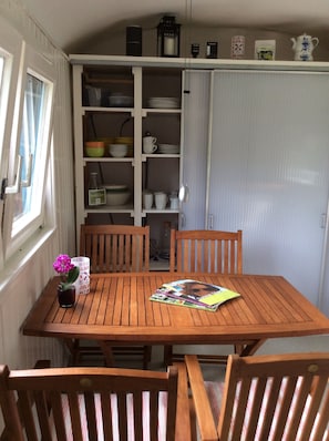 A wooden table with chairs, a potted plant, and magazines. A white cabinet with shelves is in the background. - Mobile Home 'Traumwagen An Der Mühle' with Private Terrace, Shared Garden and Wi-Fi (Nordermeldorf)