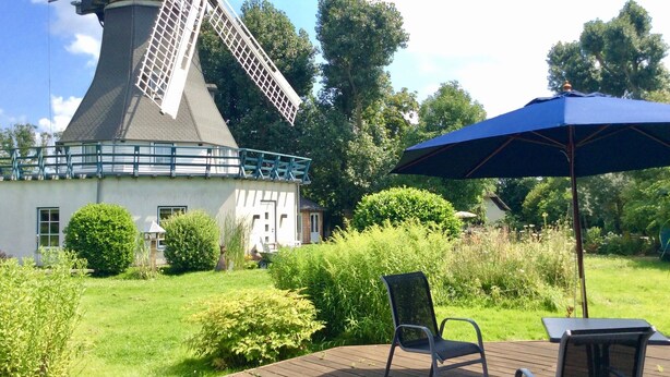 A windmill, a deck with a chair and table, and a large umbrella. - Mobile Home 'Traumwagen An Der Mühle' with Private Terrace, Shared Garden and Wi-Fi (Nordermeldorf)