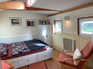 A bedroom with a bed, a chair, a radiator, a window, and a wall-mounted shelf. - Mobile Home 'Traumwagen An Der Mühle' with Private Terrace, Shared Garden and Wi-Fi (Nordermeldorf)