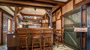 A rustic bar area with wooden chairs, a bar counter, and shelves with bottles and glasses.