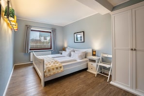 A bedroom with a bed, bedside tables, a wardrobe, a window with curtains, and a radiator. - Apartment 'Ostseeblick Fewo 1' with Private Terrace, Private Garden and Wi-Fi (Kronsgaard)