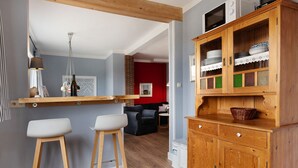 Eine Küche mit Holzhockern, einem Schrank mit Geschirr und einer roten Wand im Hintergrund.