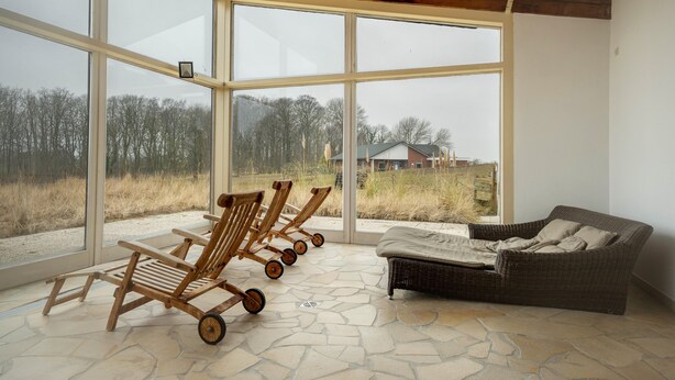 Una habitación con ventanas amplias, un sofá de mimbre y sillas de madera.