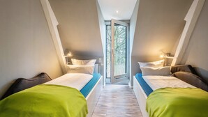 Un dormitorio con dos camas, una puerta al balcón y vista a árboles.