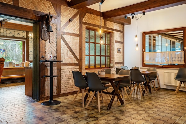Interior de un restaurante con paredes de ladrillo, vigas de madera, piso de baldosas y un comedor con mesas y sillas.