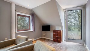 Un salón con un sofá, un televisor de pantalla plana, un mueble de madera y un ventanal con vistas a árboles.