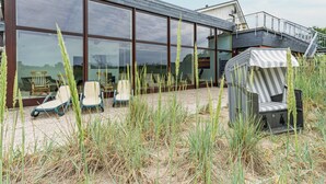 Un bâtiment moderne doté de grandes fenêtres en verre, d’une terrasse et d’un espace extérieur abrité.