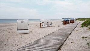Une plage avec une promenade en bois, des chaises de plage et une petite construction dotée d’auvents à rayures.