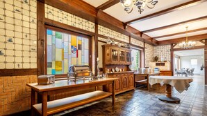 L’intérieur d’un restaurant, avec des poutres en bois, un vitrail, un espace buffet et une table ronde recouverte d’une nappe blanche.