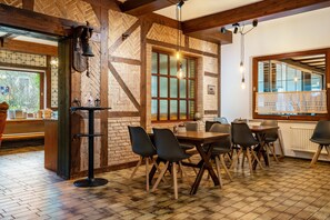 Et restaurantinteriør med murstensvægge, træbjælker, klinkegulv og et spiseområde med borde og stole.