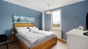 Un dormitorio con cama de madera, un escritorio, una silla, un cuadro y una ventana con vistas.