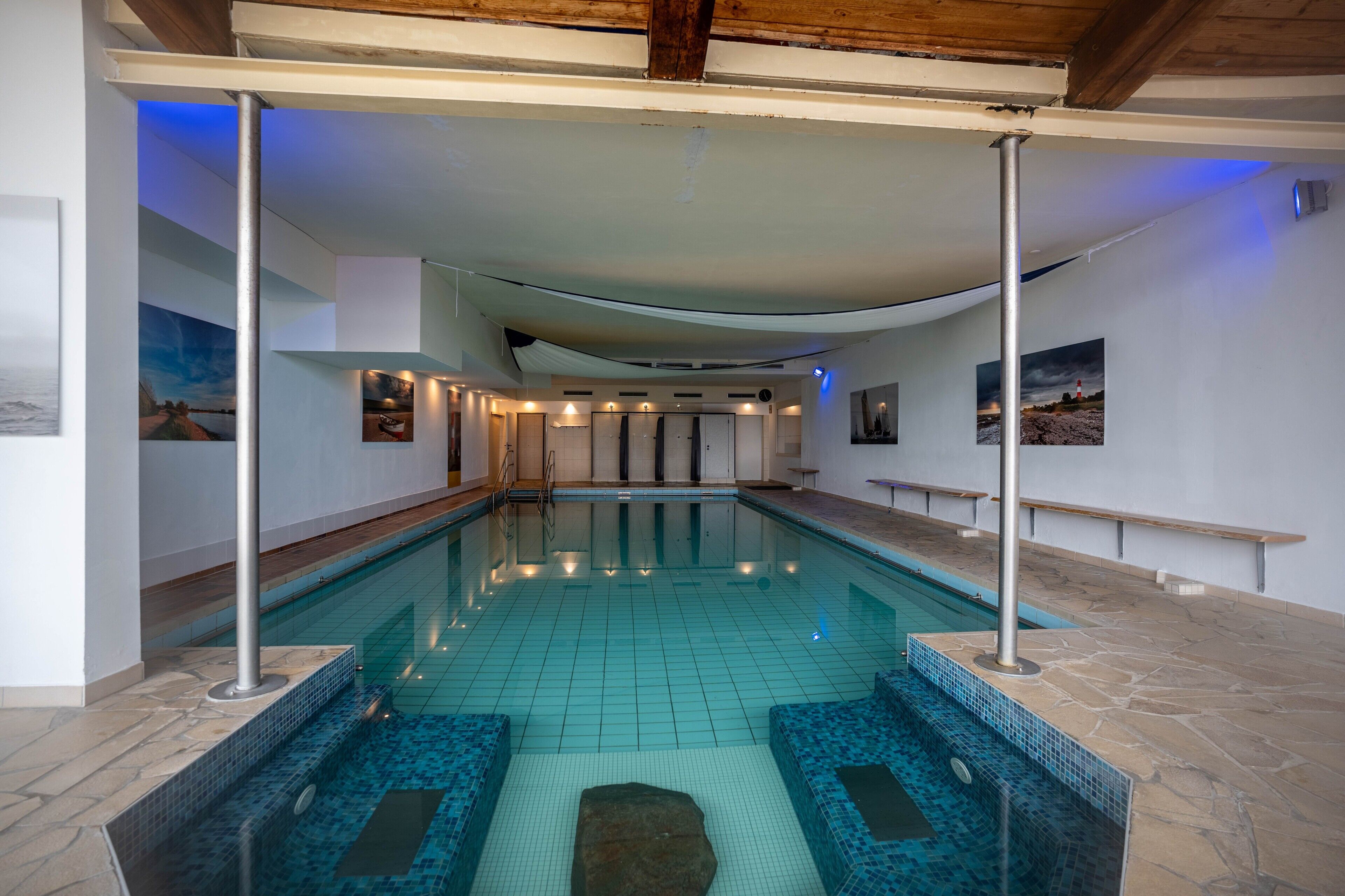 A swimming pool with tiled flooring, a wooden ceiling, and a stone-tiled edge.