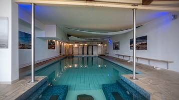 A swimming pool with tiled flooring, a wooden ceiling, and a stone-tiled edge.