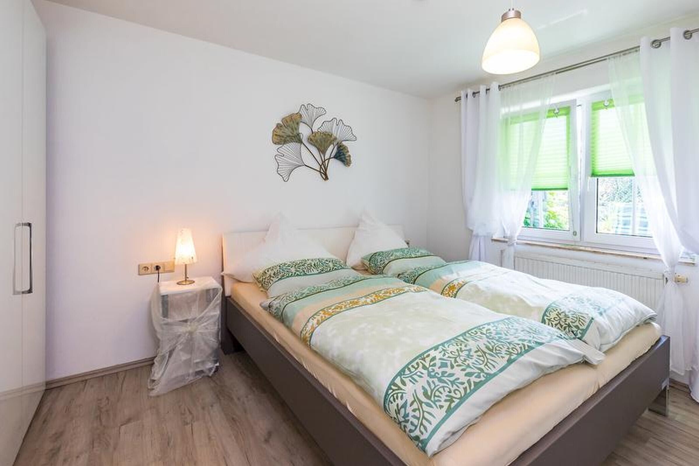 Ein Schlafzimmer mit einem Bett, einer Nachttischlampe, einer Wanddekoration und einem Fenster mit Vorhängen.