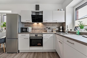 Une cuisine moderne dotée d’appareils électroménagers en acier inoxydable, de meubles blancs et d’un pare-feu en bois.