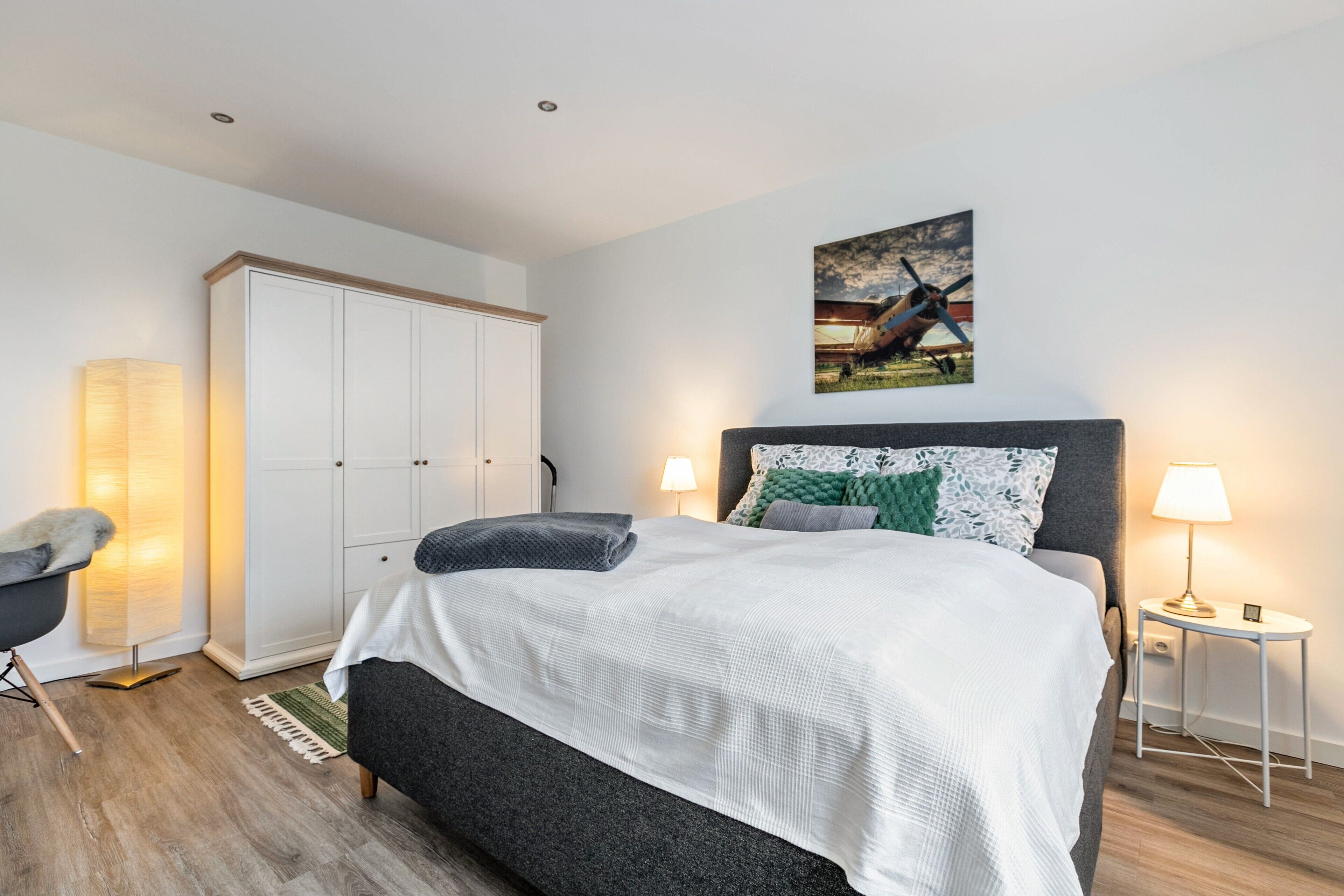 Een slaapkamer met een bed, nachtlampjes, een kledingkast en een schilderij aan de muur.