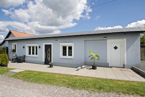 Une maison de plain-pied à l’extérieur gris, avec des boiseries blanches, un toit en tuiles, une porte d’entrée et deux fenêtres.