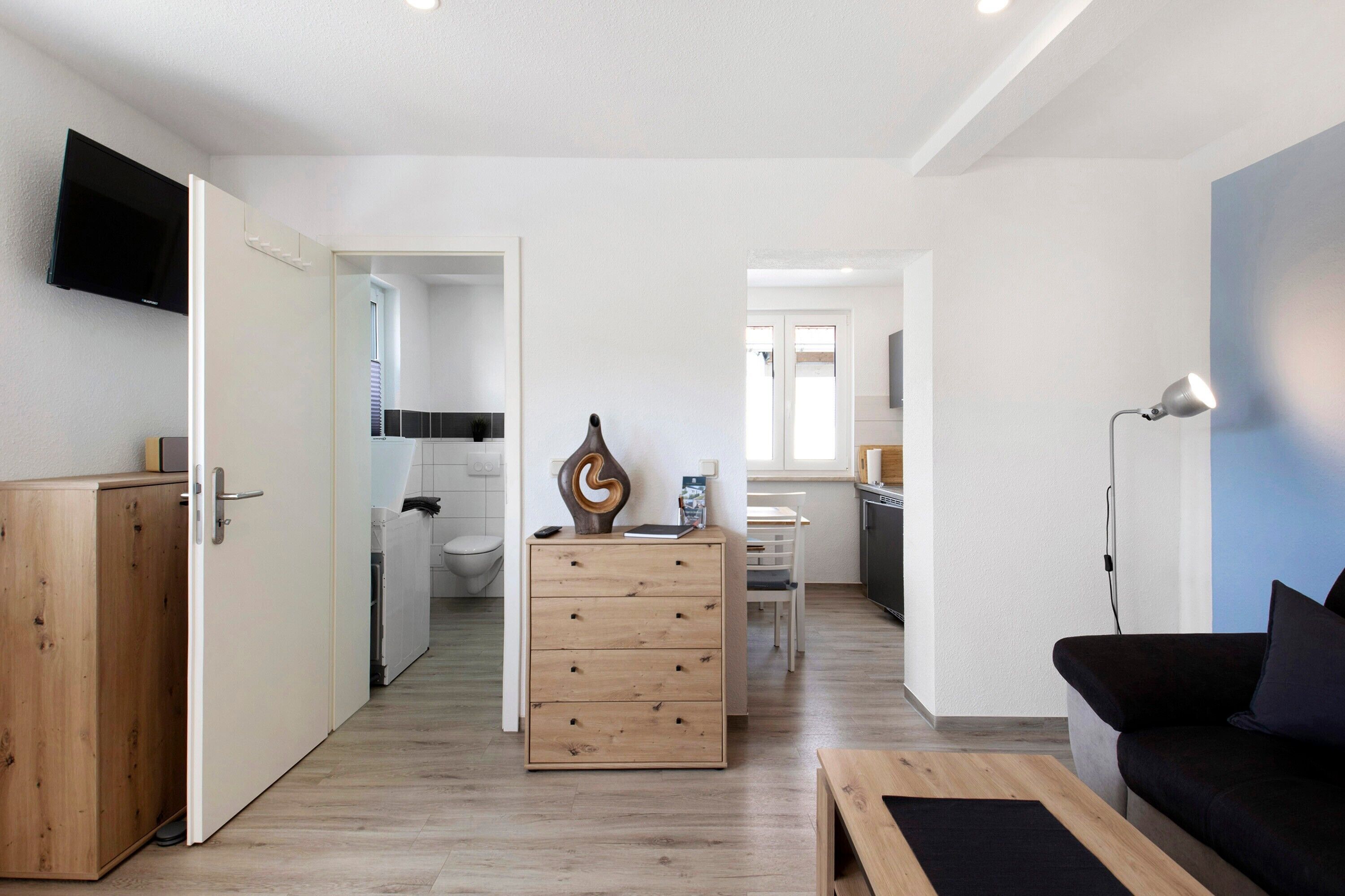 Una sala moderna con un mueble de madera, un sofá negro, una mesa de centro de madera y un escritorio con una lámpara.