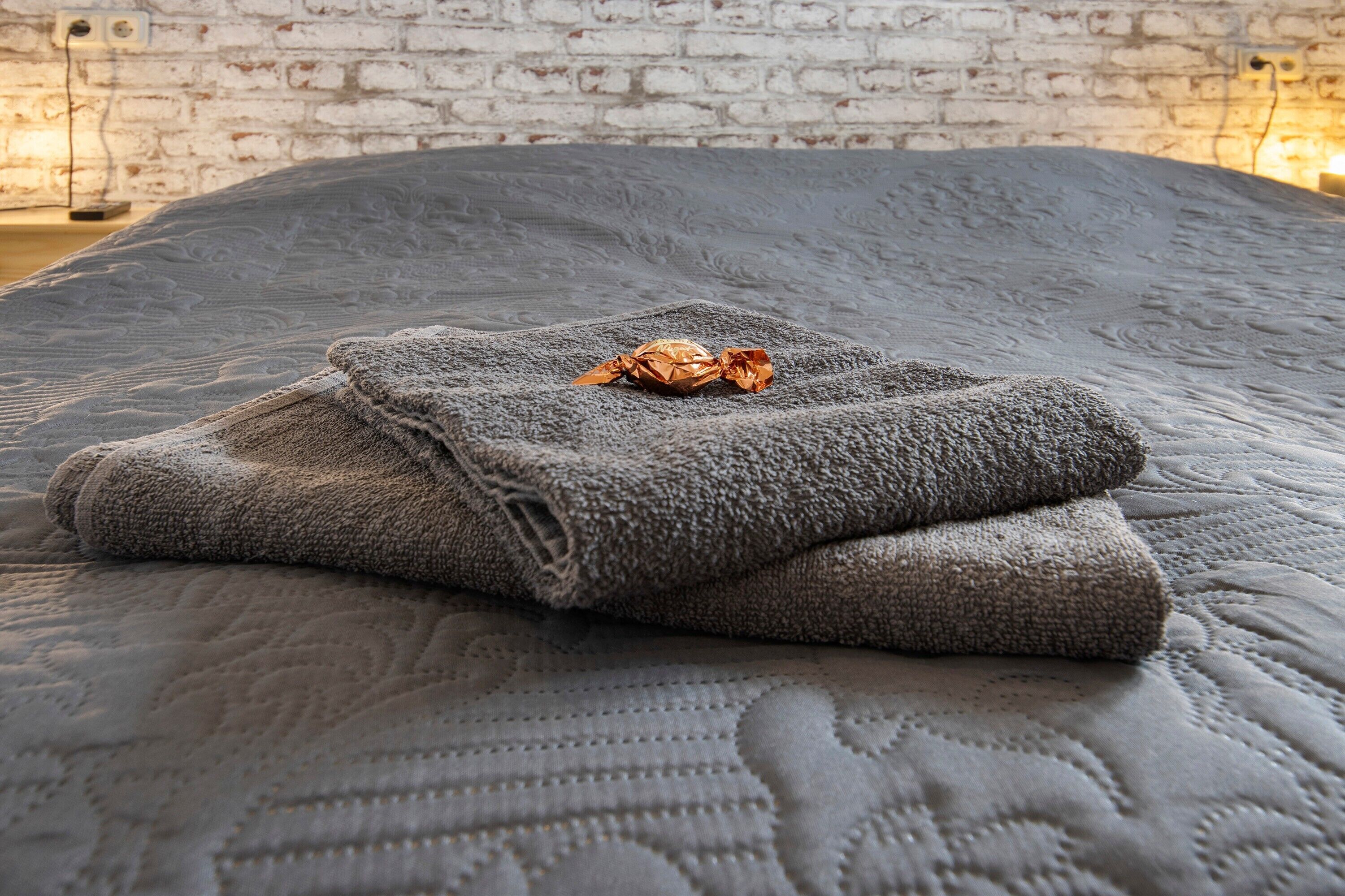 Ein Bett mit einer grauen Tagesdecke und gefalteten Handtüchern.