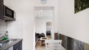 A modern kitchen with a microwave, sink, and dishwasher. A dining area with a table and chairs is visible, leading to a living room with a sofa and a small table.