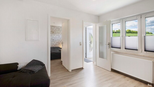 A modern interior with a sofa, a white door leading to a balcony, and a view of greenery outside.