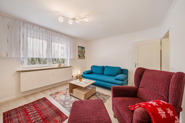 A living room with a blue sofa, a red armchair, a coffee table, and a window with curtains.